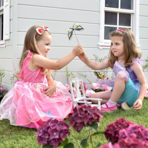 malé dievčatká v kostýmoch princezien sa hrajú pri domčeku v záhradke